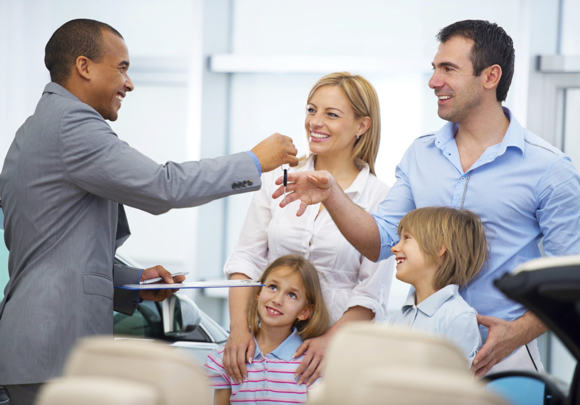 Salesperson giving a new car keys to the happy family in the showroom.